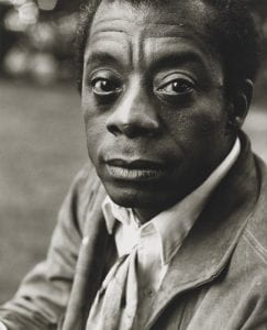 James Baldwin, a Black man, looking into the camera.