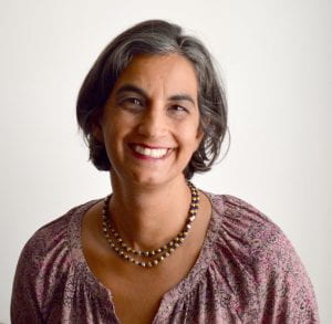 A brown-skinned woman with short grayish hair smiling