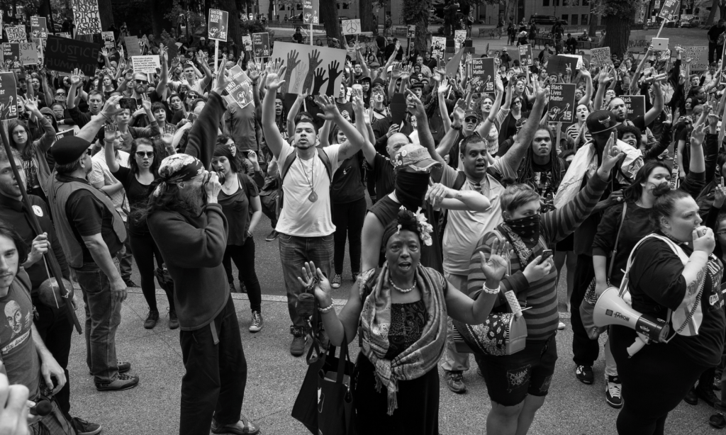 a black-and-white photo of street protests in Portland. People have their hands in the air