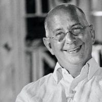 black and white photo of an older light-skinned man wearing glasses, smiling at the camera