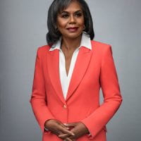 woman with brown skin and shoulder length dark hair wearing an orange blazer and white blouse